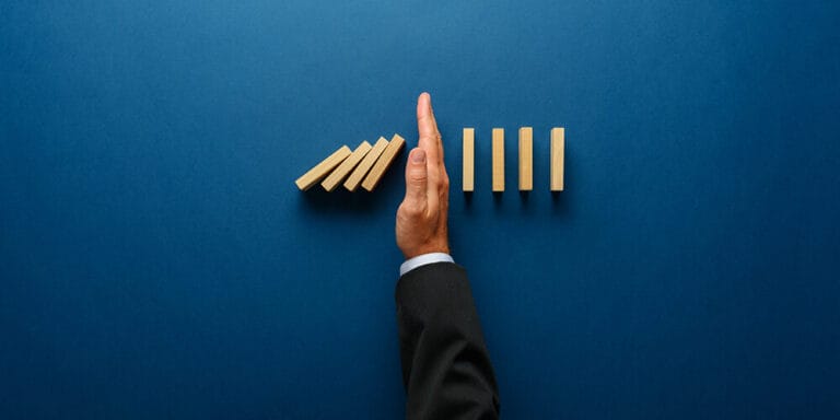 A hand separates two lines of dominos, keeping some from falling over and illustrating how crisis management tips for attorneys can help prevent additional damage.