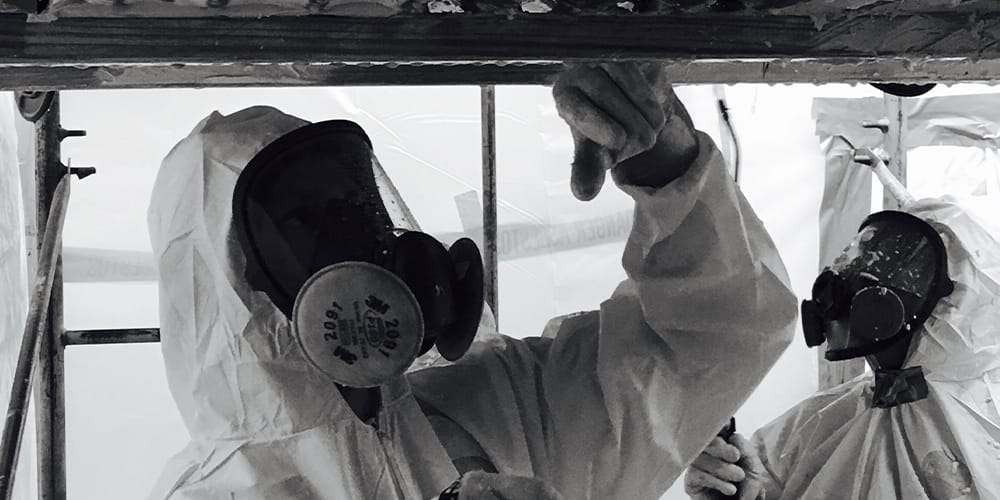 Black and white photo of a technician in a hazmat suit treating asbestos, which will lead to a remote asbestos jury trial.