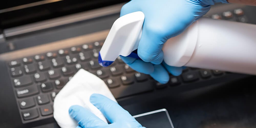 Photo of gloved hands cleaning a computer with disinfectant to avoid COVID-19, which reinforces the value of remote eDiscovery.