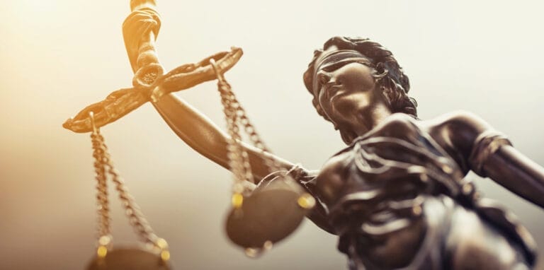 Close-up of Lady Justice, a symbol of legal fairness, featuring the balanced scales and a blindfold, against a soft-focus background with a warm glow.