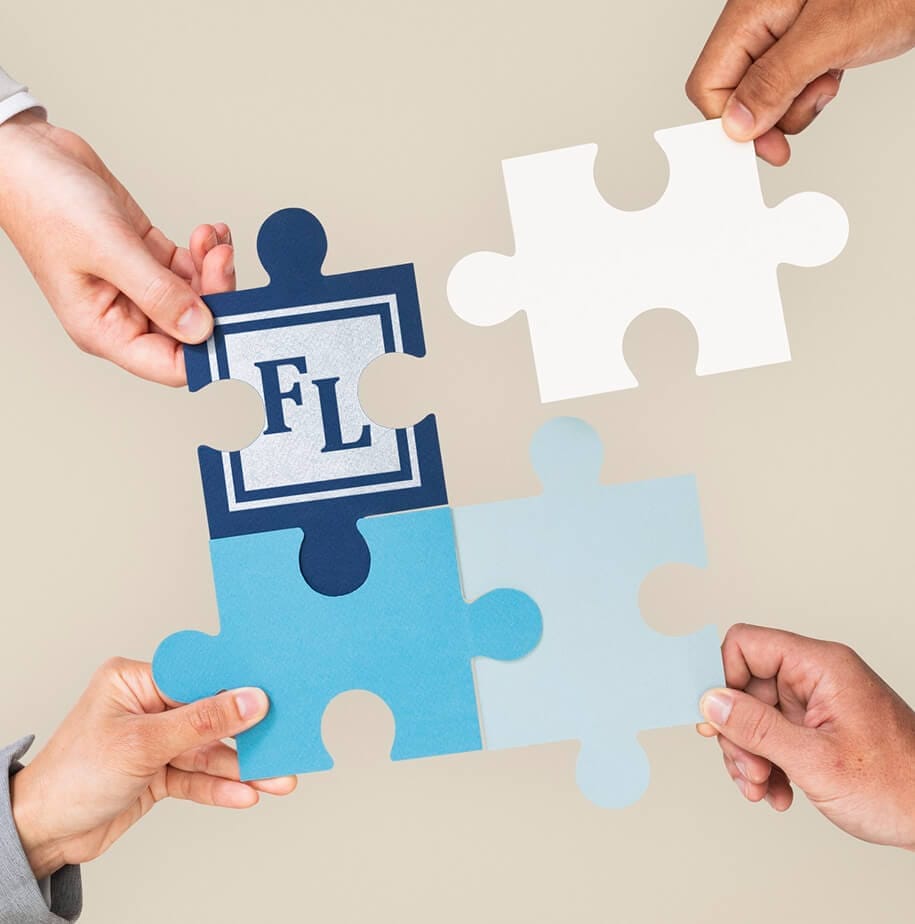 Four hands hold colorful puzzle pieces, including one with the letters "FL" against a neutral background, symbolizing teamwork.